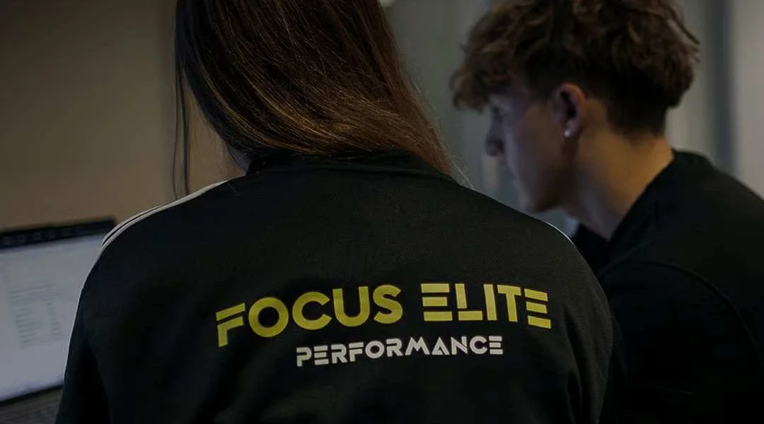 Dos alumnos estudiando frente a un portátil, uno de ellos con la chaqueta de Focus Elite Performance