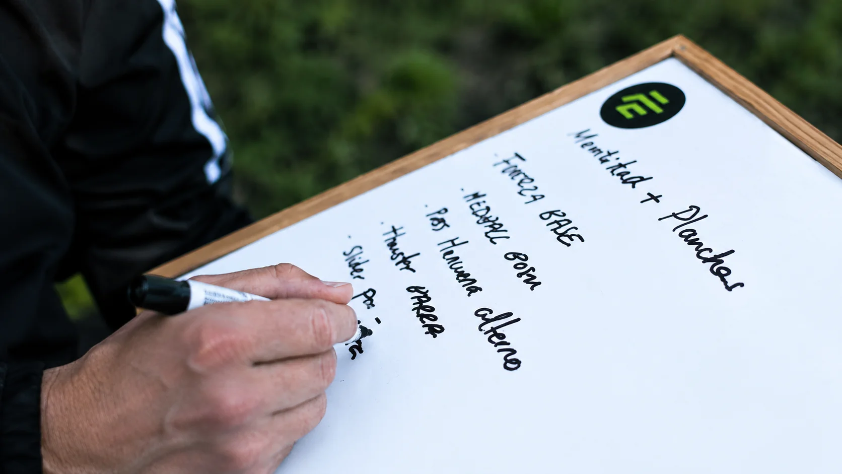 Mano escribiendo un plan de entrenamiento en una pizarra con el logo de Focus Elite