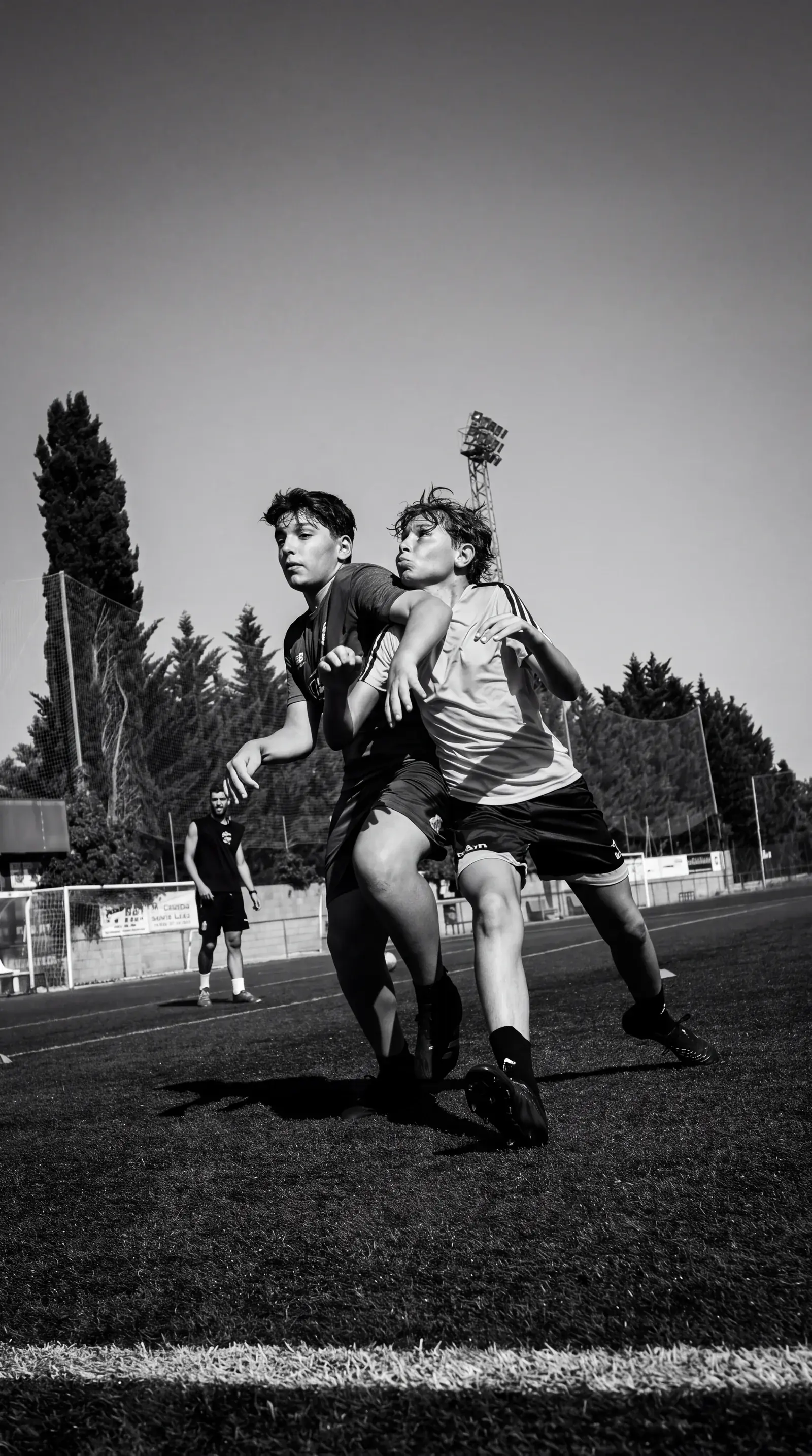 Dos jóvenes futbolistas de Focus Elite Performance compitiendo por el balón en el campo, con un entrenador observando al fondo
